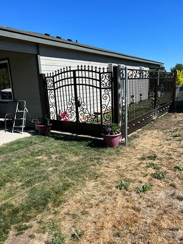 A beautifully designed fence with an elaborate ornamental iron works gate, highlighting intricate scrollwork and vertical bars. This iron works ornamental installation demonstrates the high-quality craftsmanship of structural iron and steel workers and the precision of metal pipe welding. The fence and gate provide both security and aesthetic appeal, making it an ideal solution for residential properties. The surrounding garden and lawn enhance the overall visual impact, showcasing the integration of superior fence and railing solutions. This setup exemplifies the blend of functionality and artistic design in creating elegant and durable fencing.