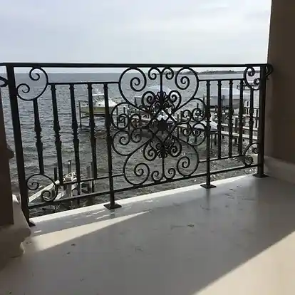 An ornate balcony railing that combines artistic ornamental iron works with superior craftsmanship. The intricate design features scrolling iron elements, creating a visually stunning iron works ornamental masterpiece. This wrought iron railing enhances the aesthetic appeal of the balcony, providing both beauty and safety. The craftsmanship involved highlights the skills of structural iron and steel workers, demonstrating their proficiency in fabricated structural steel and metal pipe welding. The balcony's design seamlessly integrates the elegance of traditional ironwork with modern construction techniques, making it a standout feature in any residential setting.