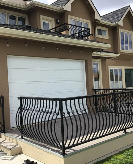 An elegant deck with railings made of intricately designed wrought iron. The curved metal bars and decorative elements add a touch of sophistication to the residential property. The railing design ensures safety while enhancing the aesthetic appeal of the outdoor space. This setup showcases the use of railings wrought iron in residential applications, providing both functionality and style. The deck is situated above a garage, demonstrating the versatility of structural iron and steel workers in creating high-quality, durable outdoor structures. The craftsmanship and attention to detail highlight the expertise involved in metal pipe welding and fabricated structural steel projects.